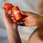 Manos sosteniendo el dōTERRA On Guard Stick con Equinácea abierto y el tapón en la otra mano.