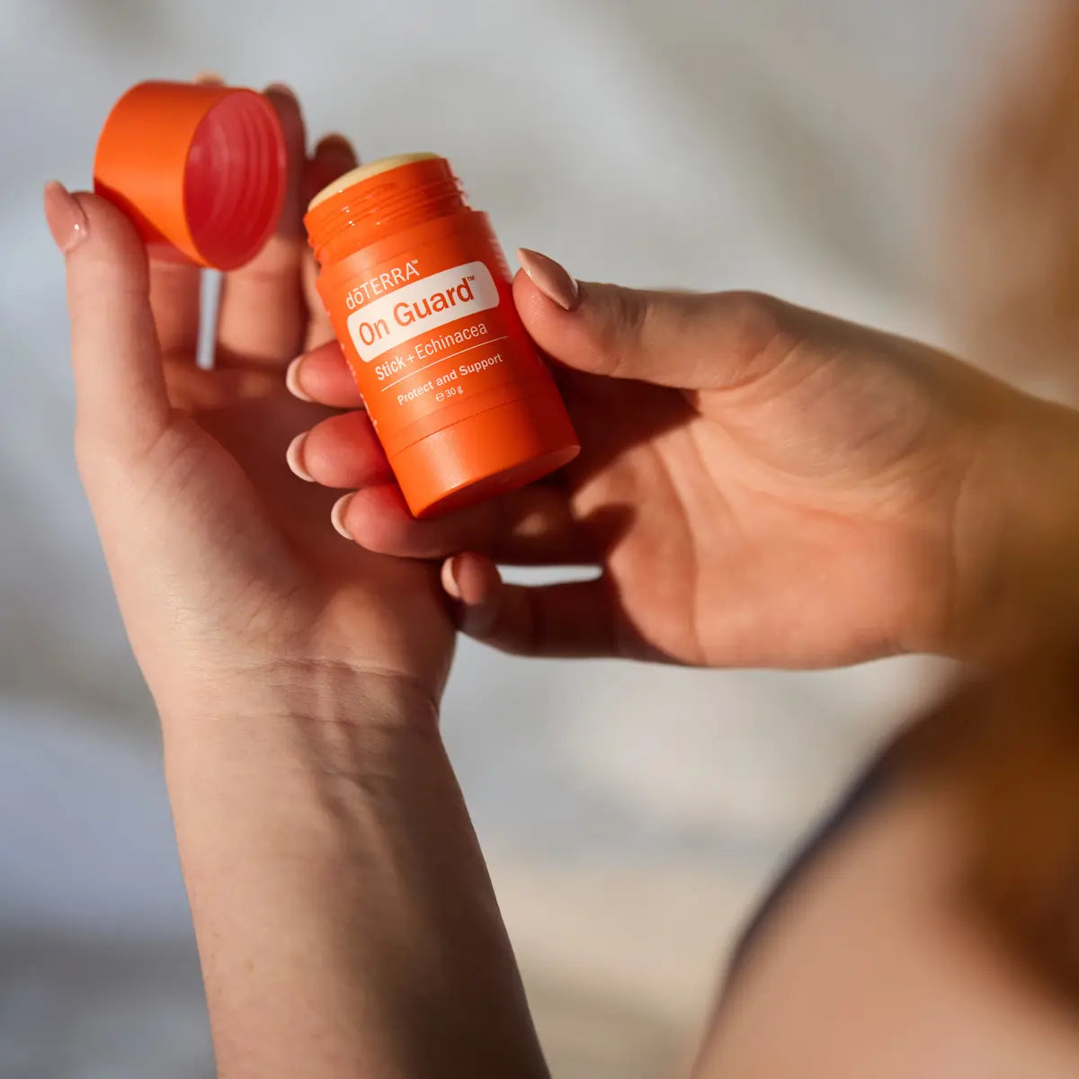 Manos sosteniendo el dōTERRA On Guard Stick con Equinácea abierto y el tapón en la otra mano.