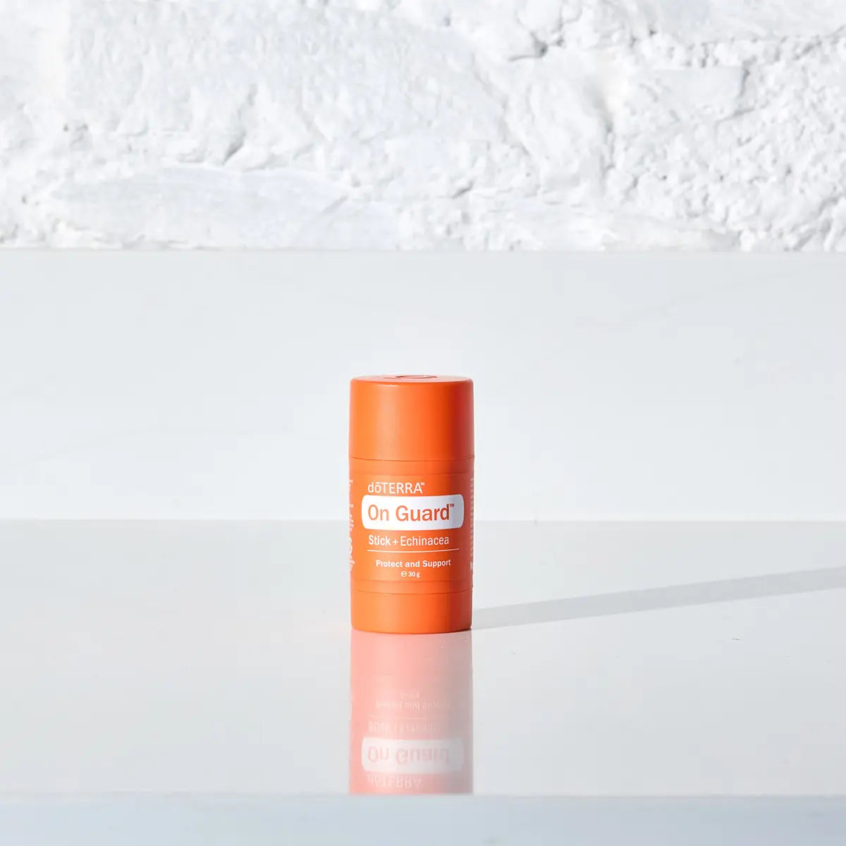 Envase dōTERRA On Guard Stick con Equinácea sobre superficie blanca reflectante y fondo neutro.