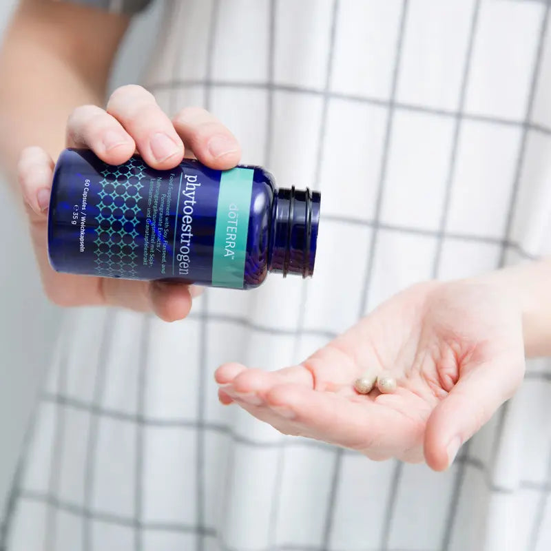 Persona vertiendo dos cápsulas de dōTERRA Phytoestrogen del frasco azul a la palma de la mano.