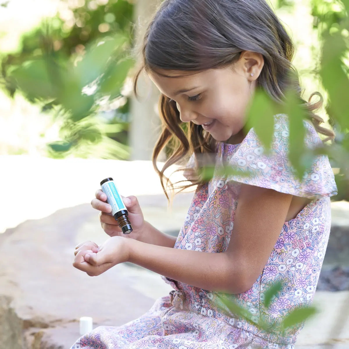 Niña con vestido floral aplicando el roll-on dōTERRA Rescuer Touch 10ml en la muñeca al aire libre.