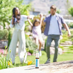 Frasco dōTERRA Rescuer Touch 10ml en primer plano con familia jugando al aire libre en el jardín desenfocada al fondo.