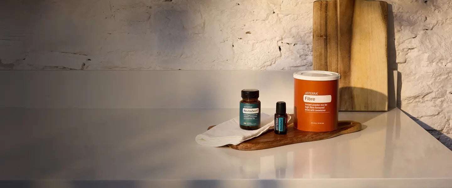 Frasco de dōTERRA RevitaZen Plus, frasco de aceite RevitaZen 15ml y bote dōTERRA Fibre sobre tabla de madera en encimera blanca.