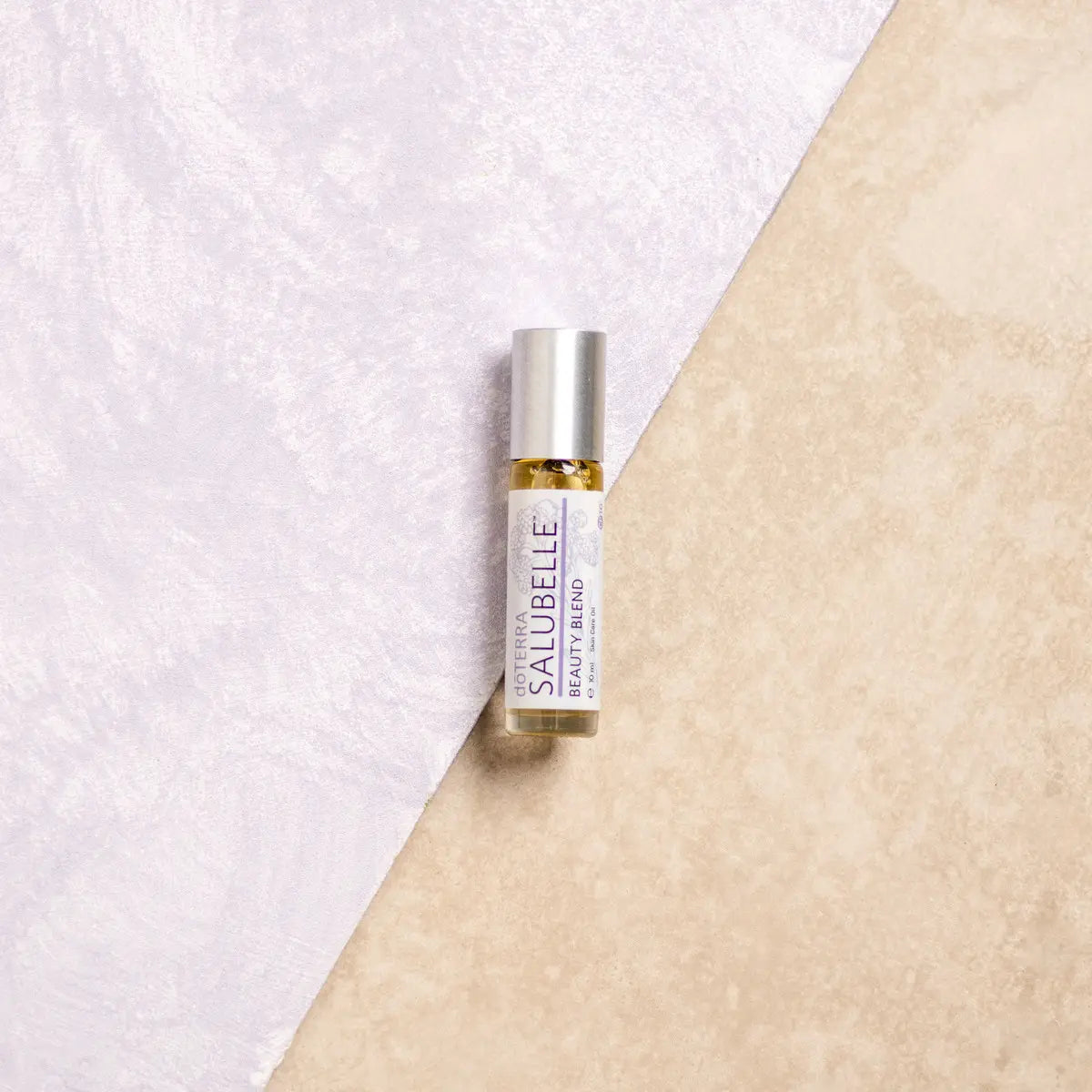 Roll-on de aceite esencial dōTERRA Salubelle Beauty Blend 10ml centrado sobre fondo bicolor lila y beige.