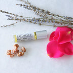 Roll-on dōTERRA Salubelle Beauty Blend 10ml acompañado por ramos de lavanda seca, pétalos de rosa rosa y piedras de resina de incienso sobre superficie blanca.
