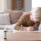 Frasco roll-on dōTERRA Steady Touch 10ml en primer plano con niño dibujando desenfocado al fondo.