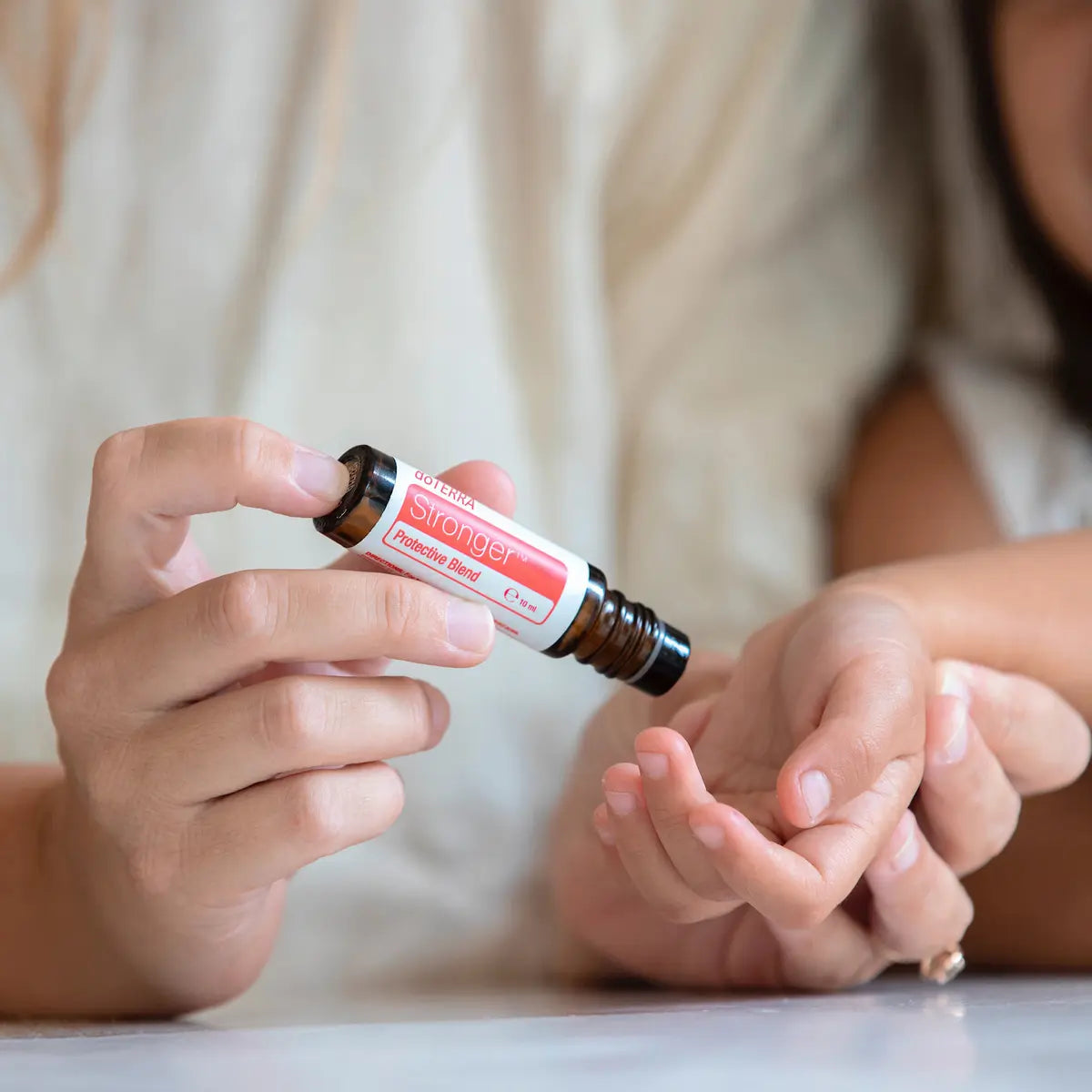Adulto aplicando el roll-on dōTERRA Stronger Touch de 10ml en la mano de un niño.