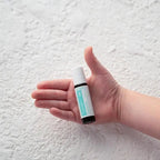 Mão de criança a segurar o frasco roll-on dōTERRA Tamer Touch de 10ml sobre fundo branco com textura.