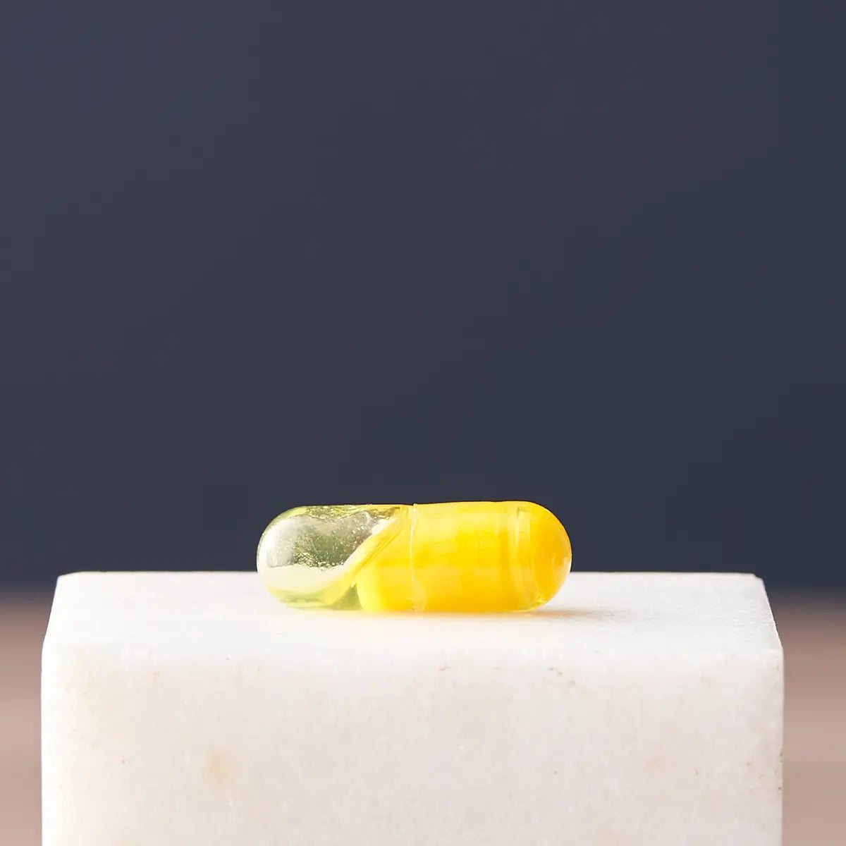 Detalle en primer plano de una cápsula de doble cámara dōTERRA Turmeric sobre bloque de mármol blanco