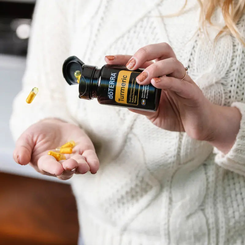 Mano vertiendo cápsulas amarillas de dōTERRA Turmeric Dual Chamber del frasco oscuro a la palma de la mano.