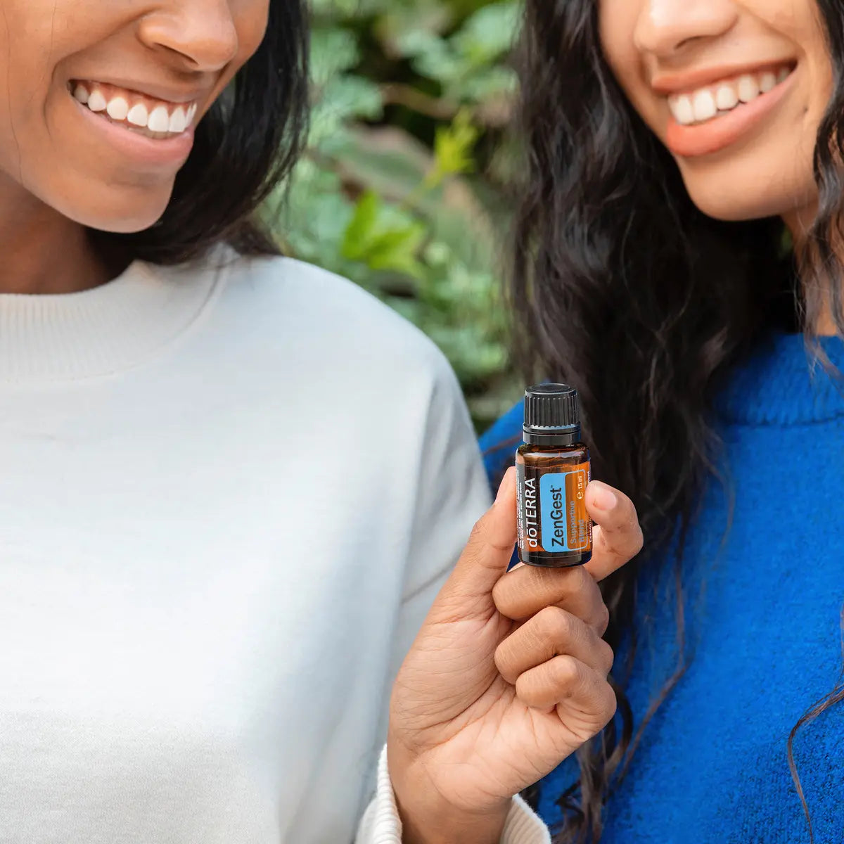 Mano sosteniendo el frasco de dōTERRA ZenGest 15ml con dos mujeres sonrientes en segundo plano.