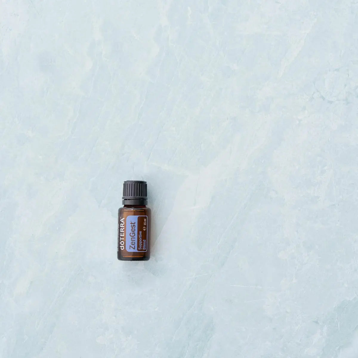Frasco de aceite esencial dōTERRA ZenGest 15ml centrado sobre fondo de mármol azul claro.