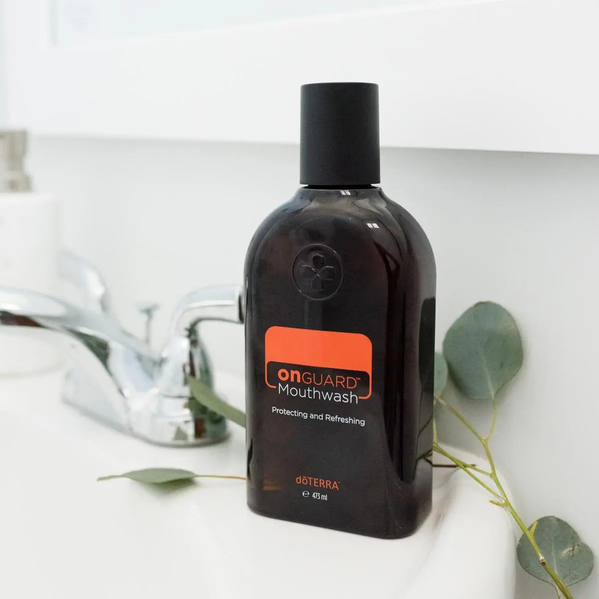 Enjuague bucal On Guard dōTERRA 473ml — frasco sobre encimera de baño con eucalipto