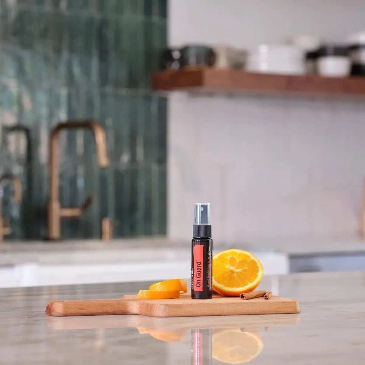 Espray purificador On Guard dōTERRA 27ml — frasco sobre tabla de cocina con naranja y canela