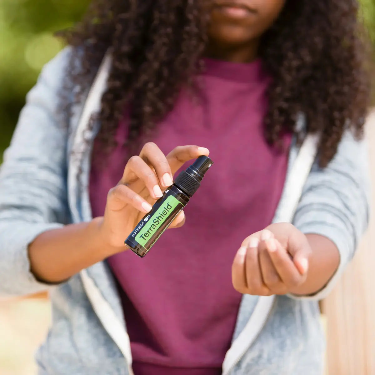 Espray dōTERRA TerraShield 30ml — niña de pelo rizado aplicándolo en la muñeca en el jardín al exterior