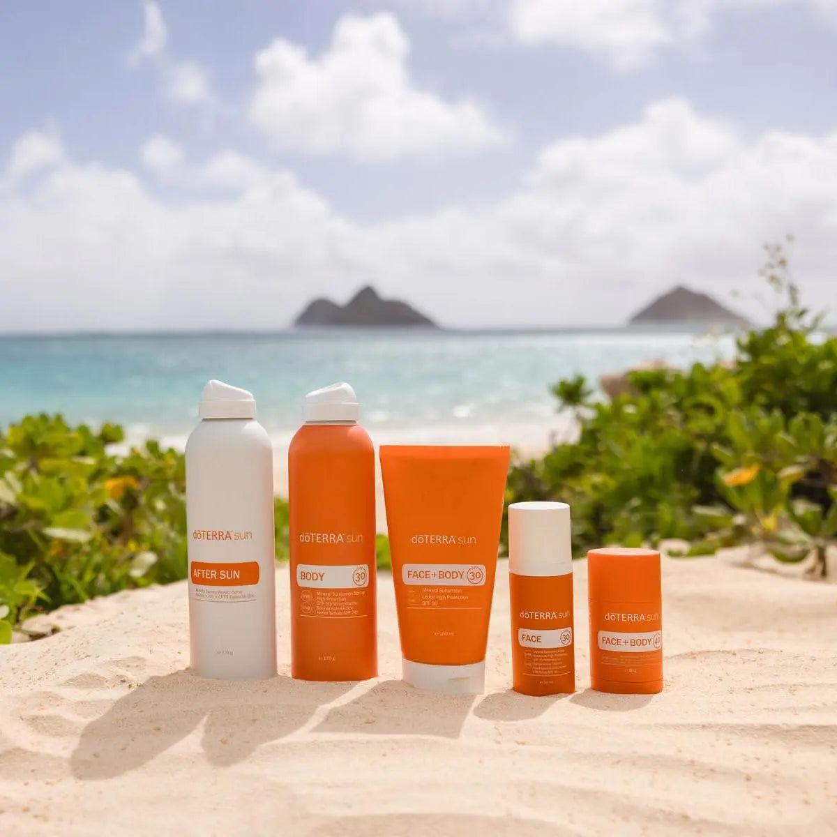 Gama Sun dōTERRA — productos completos en playa con arena, mar e isla tropical al fondo
