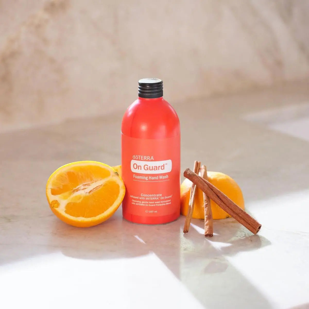 Limpiador concentrado On Guard dōTERRA 237ml — frasco sobre mármol con naranja y canela