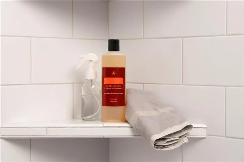 Limpiador concentrado On Guard™ dōTERRA 355ml en estantería de baño con azulejos y pulverizador