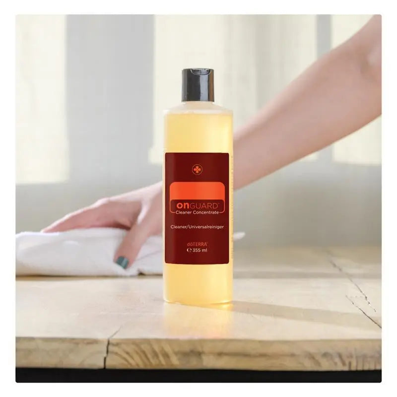 Limpiador concentrado On Guard™ dōTERRA 355ml en primer plano con mano limpiando superficie de madera