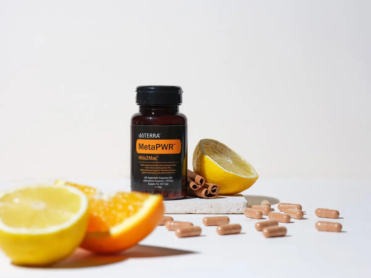 MetaPWR Mito2Max doTERRA en estudio con naranjas cortadas, limon, palos de canela y capsulas beige esparcidas sobre fondo blanco