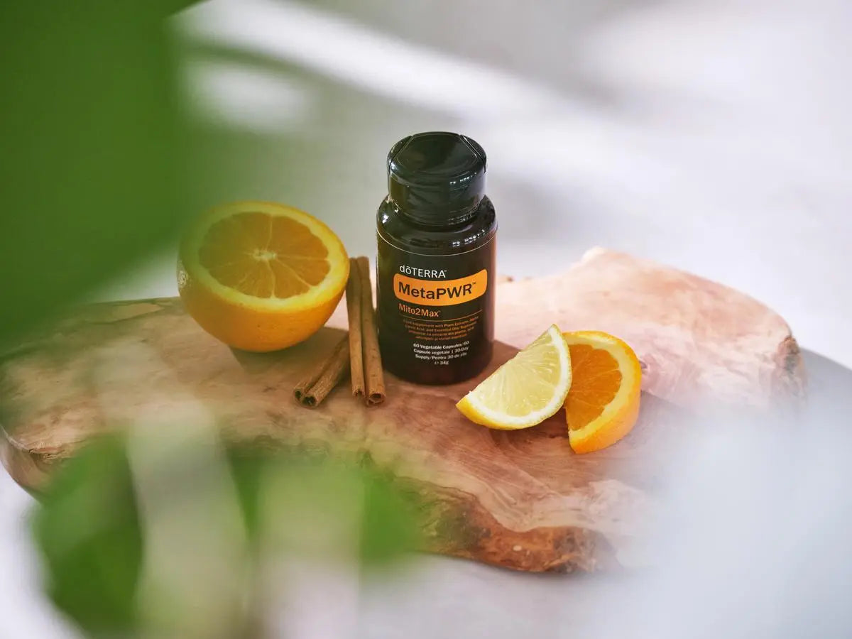 MetaPWR Mito2Max doTERRA sobre rodaja de madera natural con media naranja, gajos de limon y ramas de canela, planta verde en primer plano