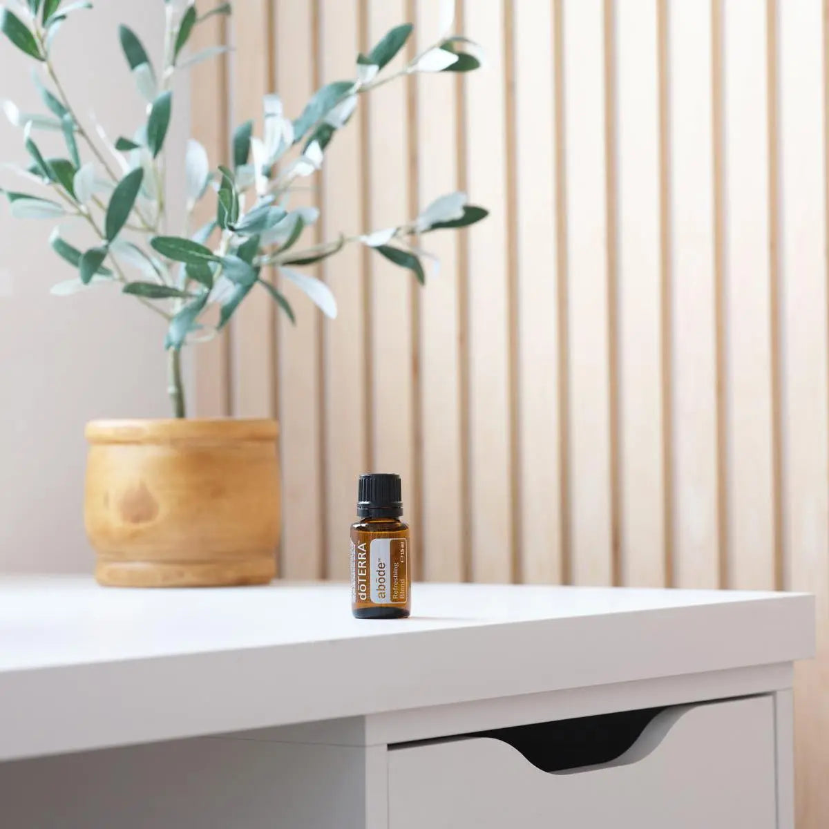 Mezcla Abode dōTERRA 15ml sobre escritorio blanco con maceta en panel de lamas de madera