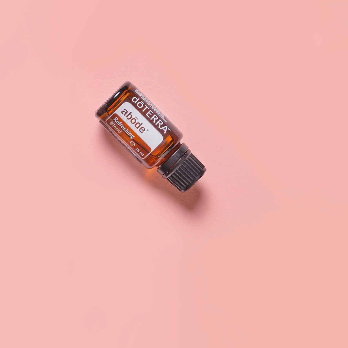 Mezcla Abode dōTERRA 15ml frasco inclinado sobre fondo rosa coral vibrante