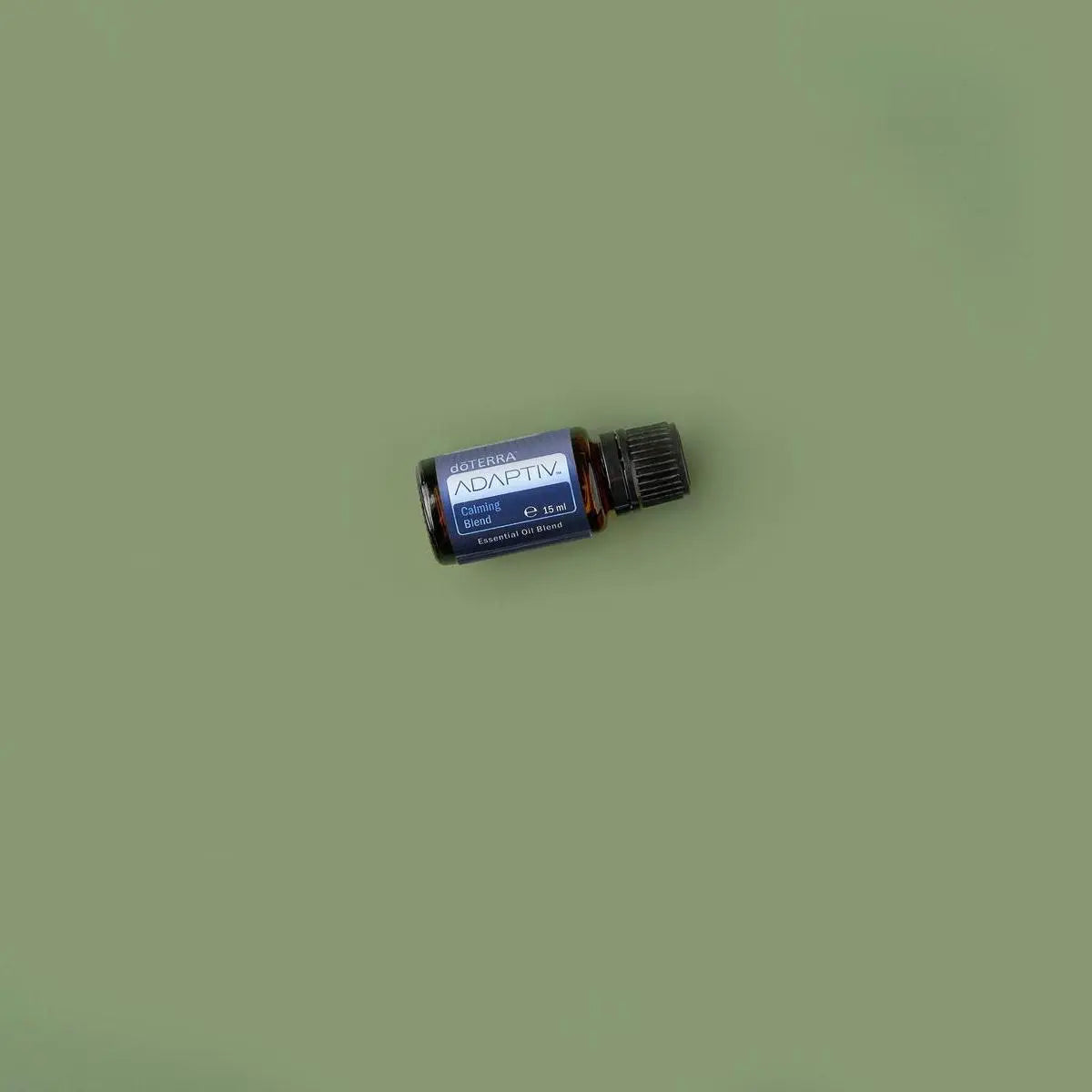 Mezcla Adaptiv dōTERRA 15ml, frasco inclinado sobre fondo verde oliva, cenital de estudio