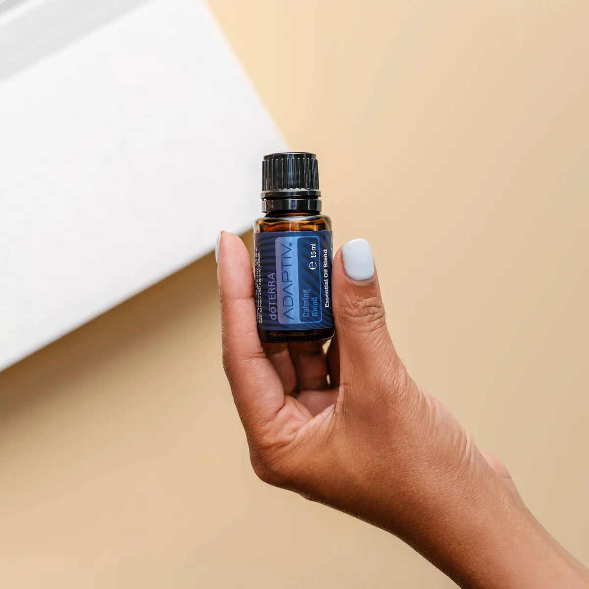 Mano de piel oscura sosteniendo el frasco de Mezcla Adaptiv dōTERRA 15ml sobre fondo beige