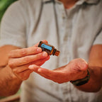 Hombre con camisa blanca abriendo el frasco de Mezcla Air dōTERRA 15ml en exterior con bokeh verde