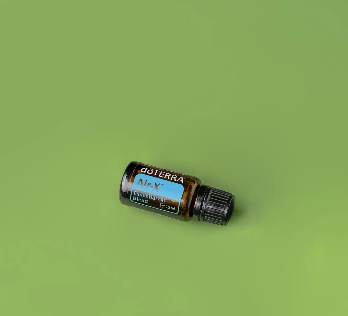 Mezcla Air-X dōTERRA 15ml, frasco inclinado sobre fondo verde oliva, fotografía cenital de estudio