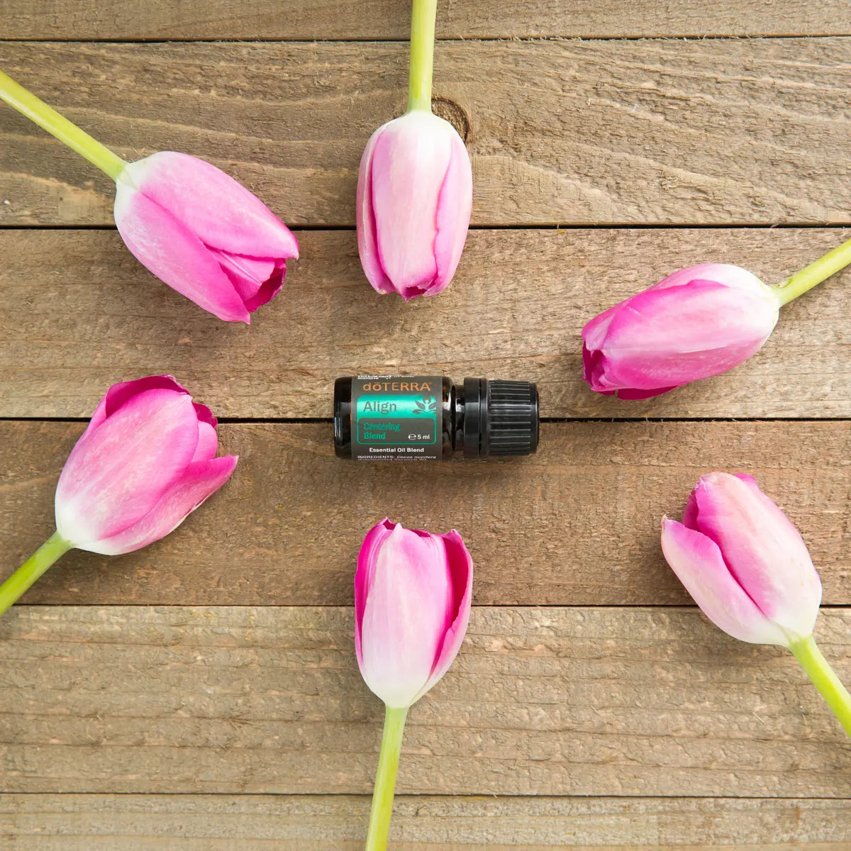 Frasco de Mezcla Align dōTERRA 5ml sobre tabla de madera rústica rodeado de tulipanes rosas, cenital
