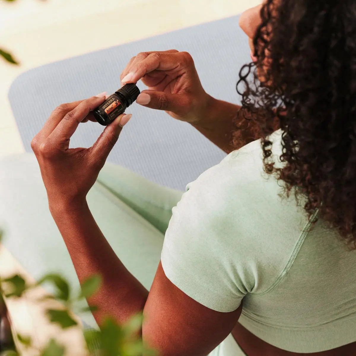 Mezcla dōTERRA Arise 5ml — mujer de piel oscura sosteniendo el frasco sobre esterilla de yoga azul