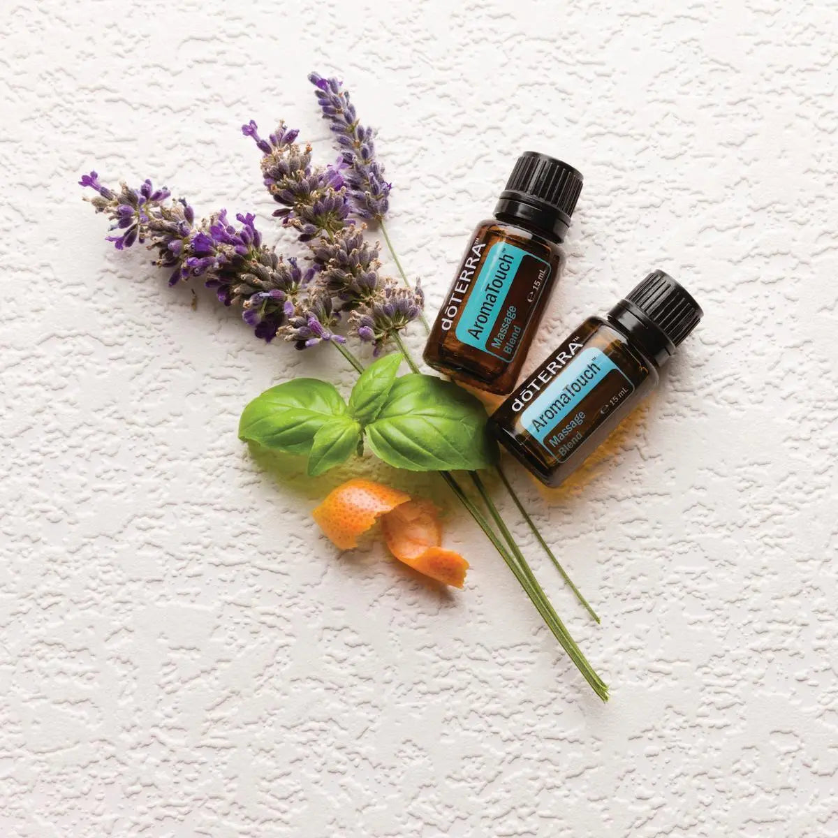 Mezcla dōTERRA AromaTouch 15ml — dos frascos con lavanda, albahaca y naranja sobre superficie rugosa