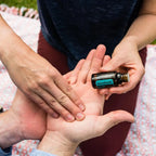 Mezcla dōTERRA AromaTouch 15ml — dos personas compartiendo un masaje en la mano al exterior con manta floral