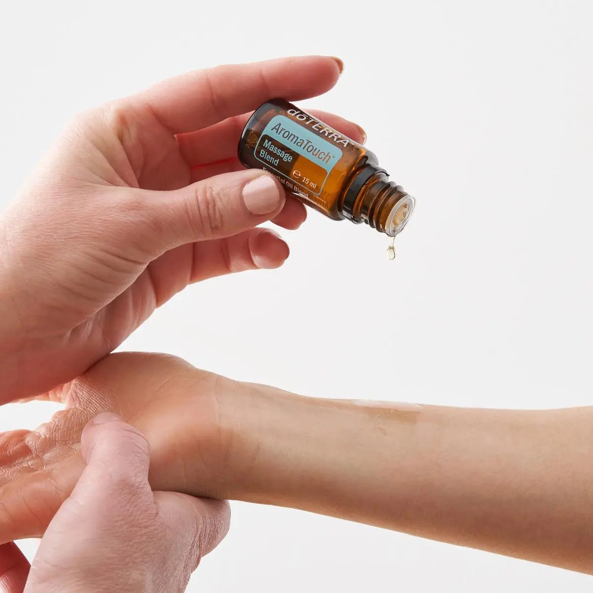 Mezcla dōTERRA AromaTouch 15ml — manos aplicando una gota en la muñeca durante un masaje, fondo blanco