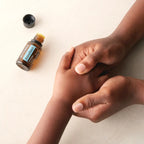 Mezcla dōTERRA AromaTouch 15ml — manos de piel oscura realizando masaje en la palma, fondo beige
