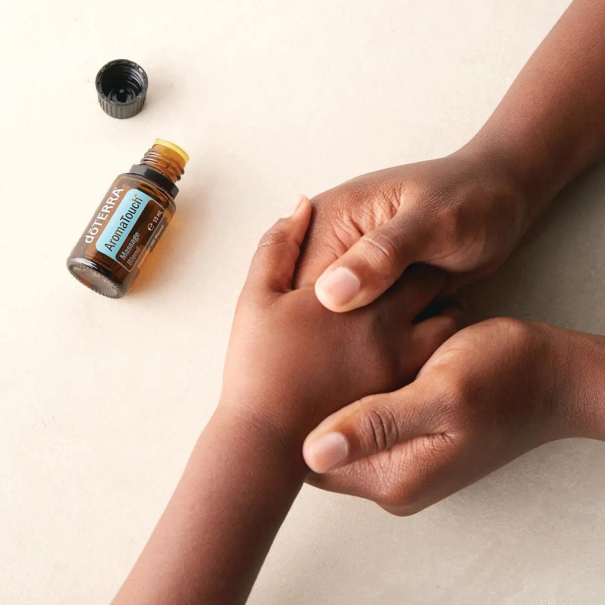 Mezcla dōTERRA AromaTouch 15ml — manos de piel oscura realizando masaje en la palma, fondo beige
