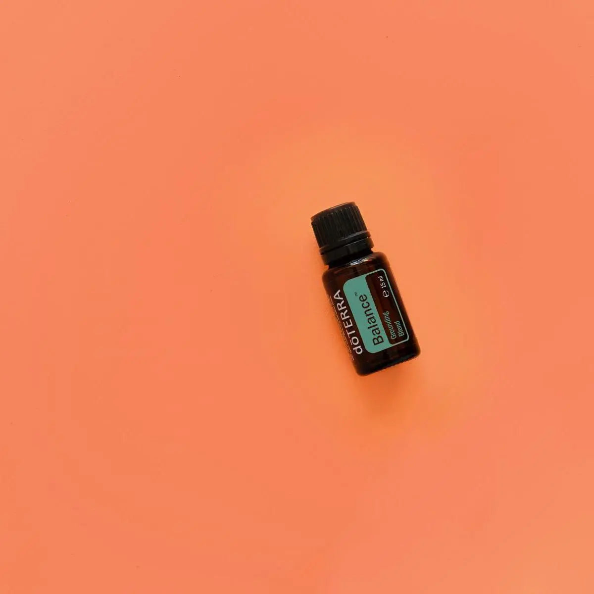Mezcla dōTERRA Balance 15ml — frasco inclinado sobre fondo naranja coral, vista cenital
