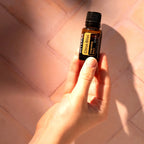 Mezcla dōTERRA Citrus Bliss 15ml — mano sosteniendo el frasco sobre suelo de mosaico de terracota con luz solar