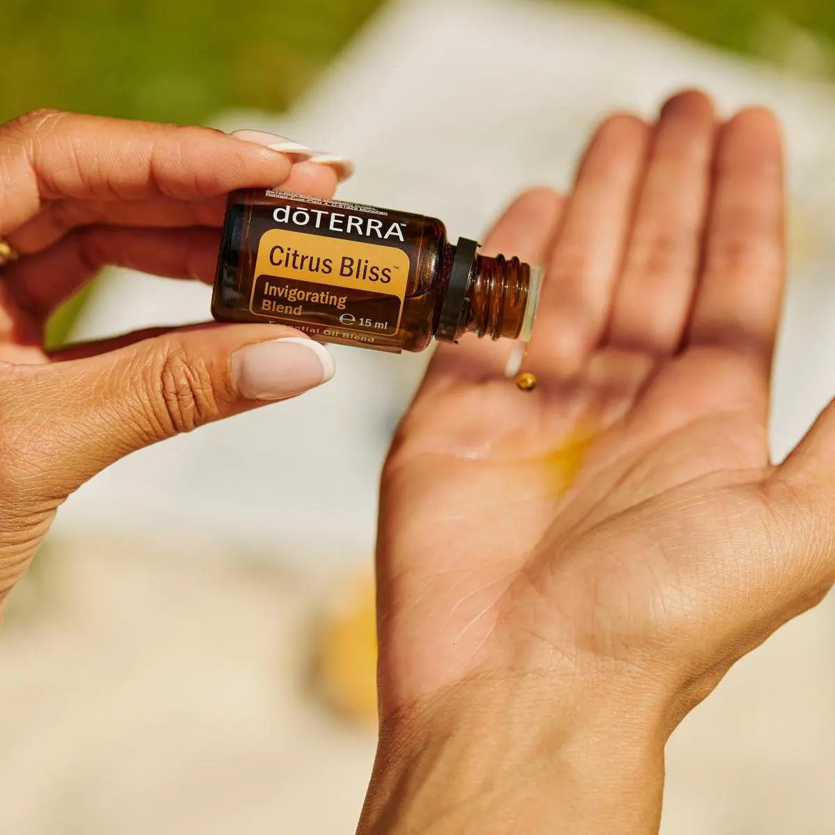 Mezcla dōTERRA Citrus Bliss 15ml — manos echando una gota en la palma al exterior con bokeh verde