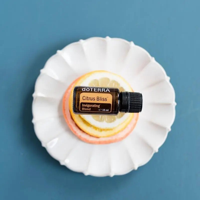 Mezcla dōTERRA Citrus Bliss 15ml — plato blanco con rodajas de limón y pomelo sobre fondo azul, vista cenital