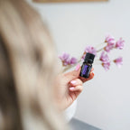 Mezcla dōTERRA Console 5ml — mano con uñas rosas sosteniendo el frasco junto a magnolia rosa
