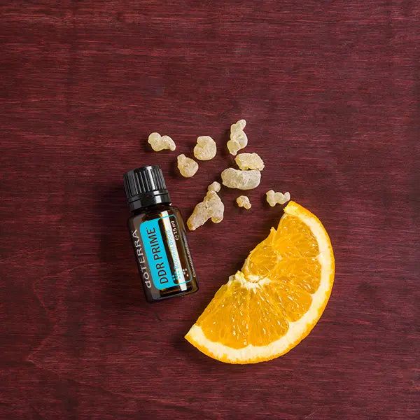 Mezcla dōTERRA DDR Prime 15ml — frasco sobre madera burdéos con rodaja de naranja y cristales de resina