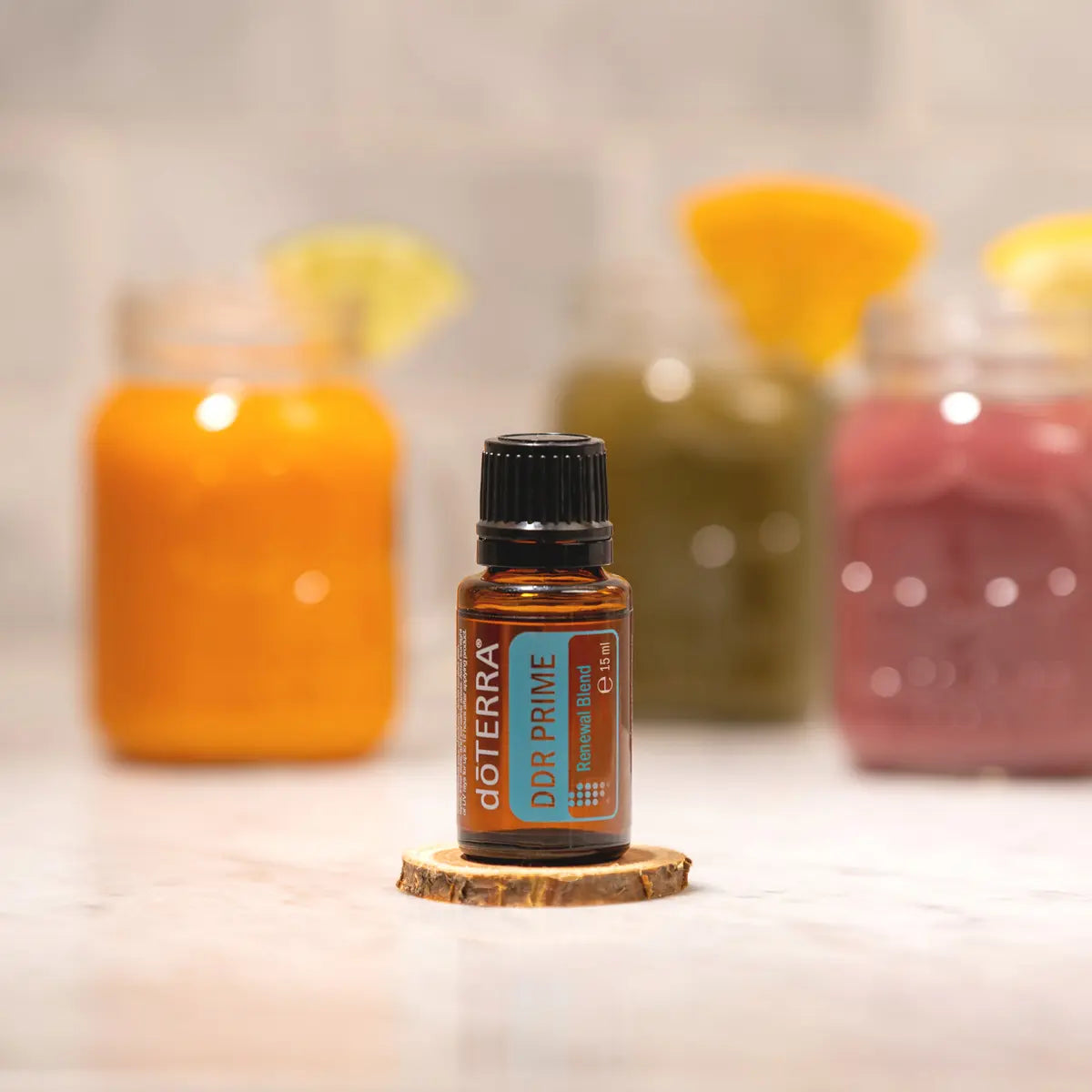 Mezcla dōTERRA DDR Prime 15ml — frasco en posavasos de madera rodeado de zumos de naranja, verde y rojo