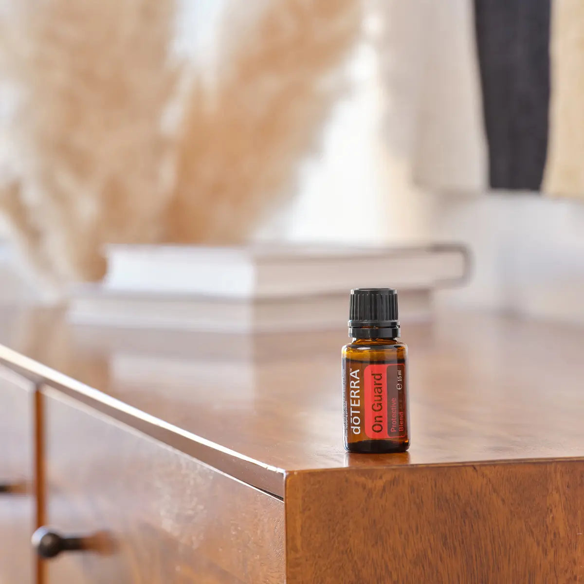 Mezcla dōTERRA On Guard 15ml — frasco sobre cómoda de madera vintage con cojines y plantas secas en bokeh