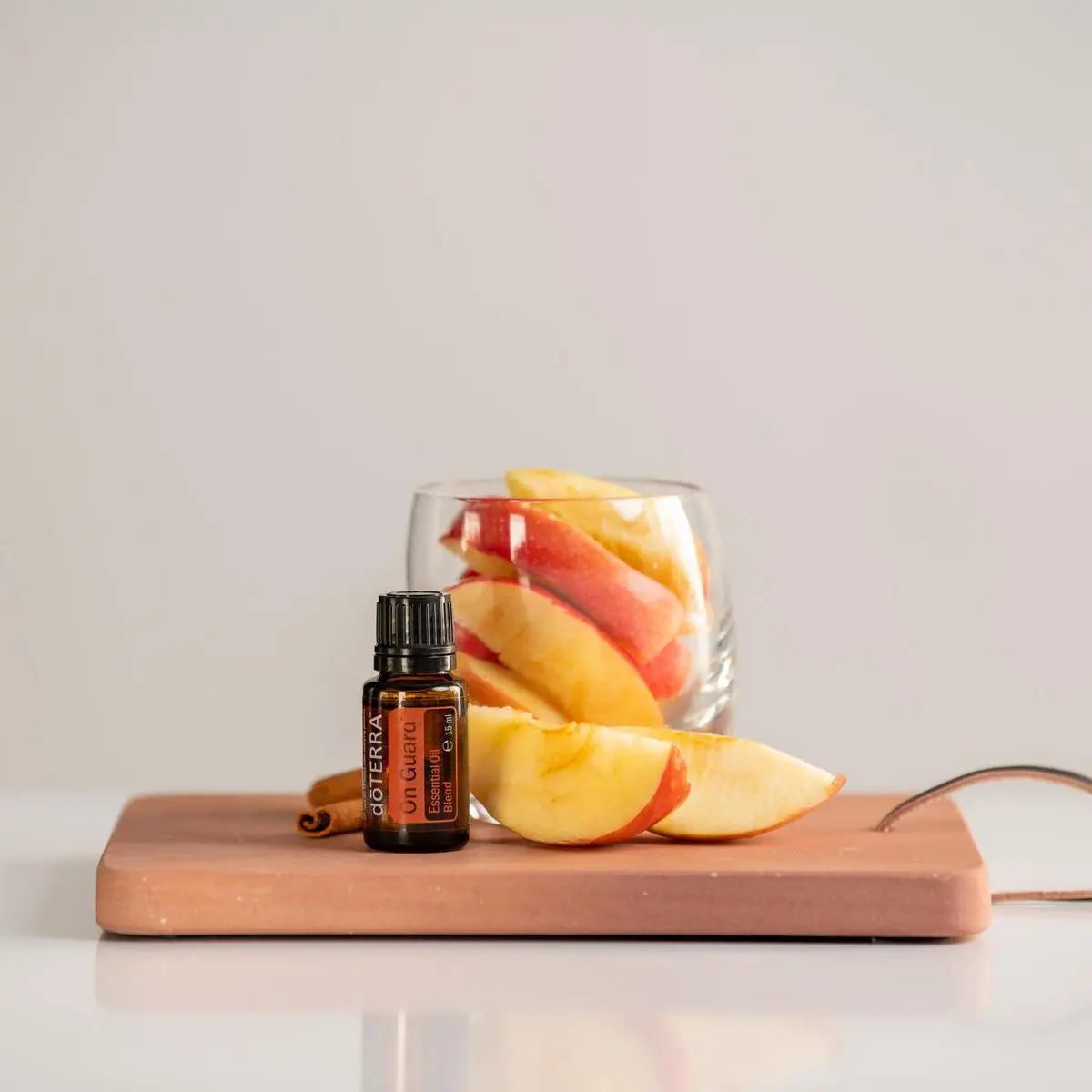 Mezcla dōTERRA On Guard 15ml — frasco sobre tabla de terracota con gajos de manzana roja, canela y vaso