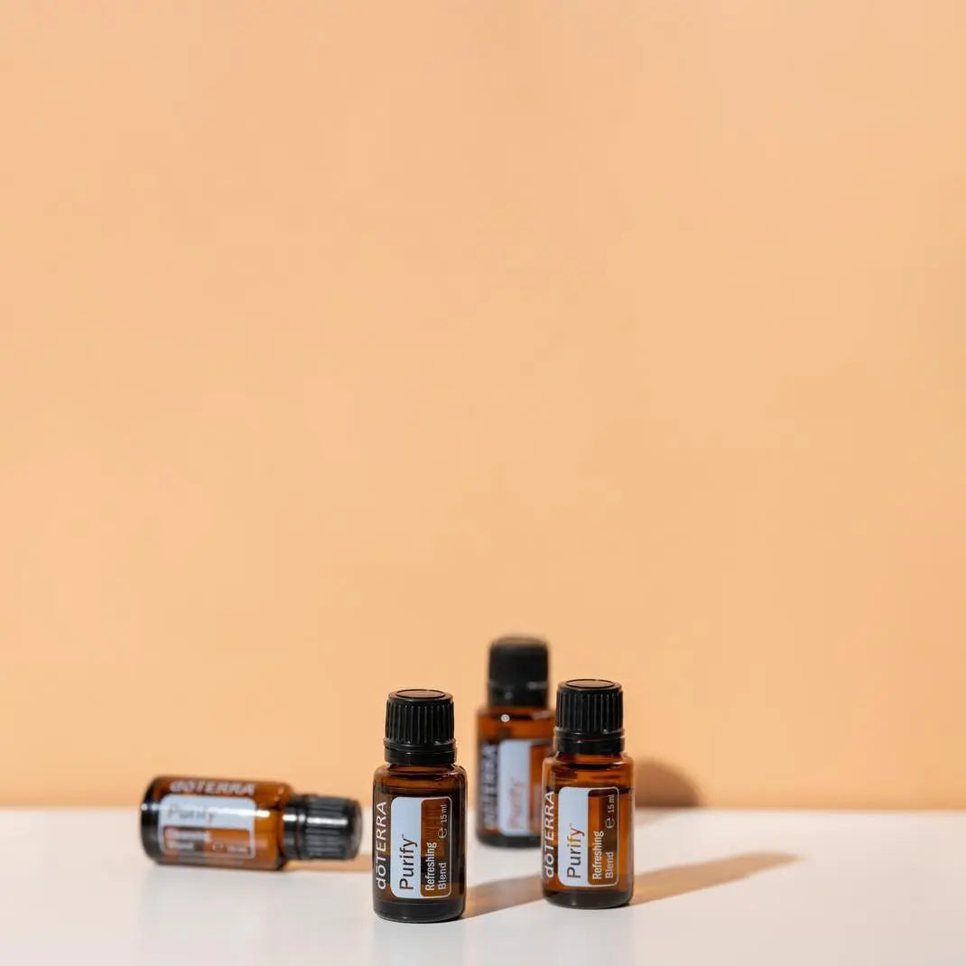 Mezcla dōTERRA Purify 15ml — cuatro frascos escalonados sobre superficie blanca y fondo naranja