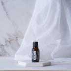 Mezcla dōTERRA Purify 15ml — frasco en posavasos cerámico hexagonal sobre tela blanca y fondo de mármol