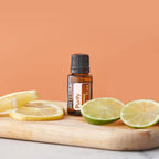 Mezcla dōTERRA Purify 15ml — frasco en tabla de madera con rodajas de limón y lima sobre fondo naranja melocotón